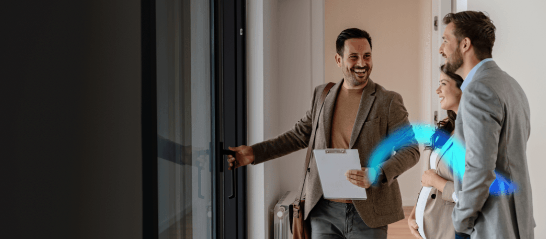 A real-estate agent smiling and gesturing toward a couple during a home walk-through; a glowing arc of light highlights the moment.